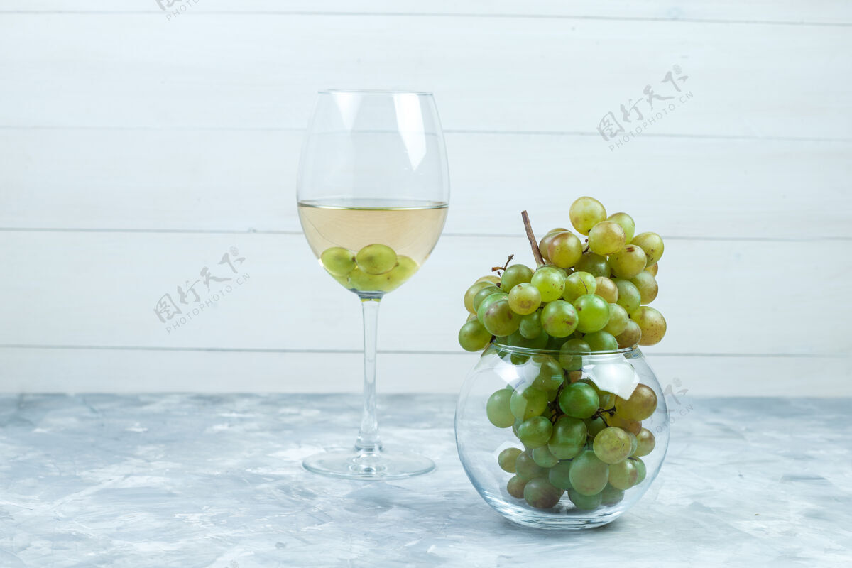 果汁一杯葡萄酒和绿色葡萄放在一个玻璃罐里 背景是灰色和木质的 侧面视图葡萄藤自然咕噜