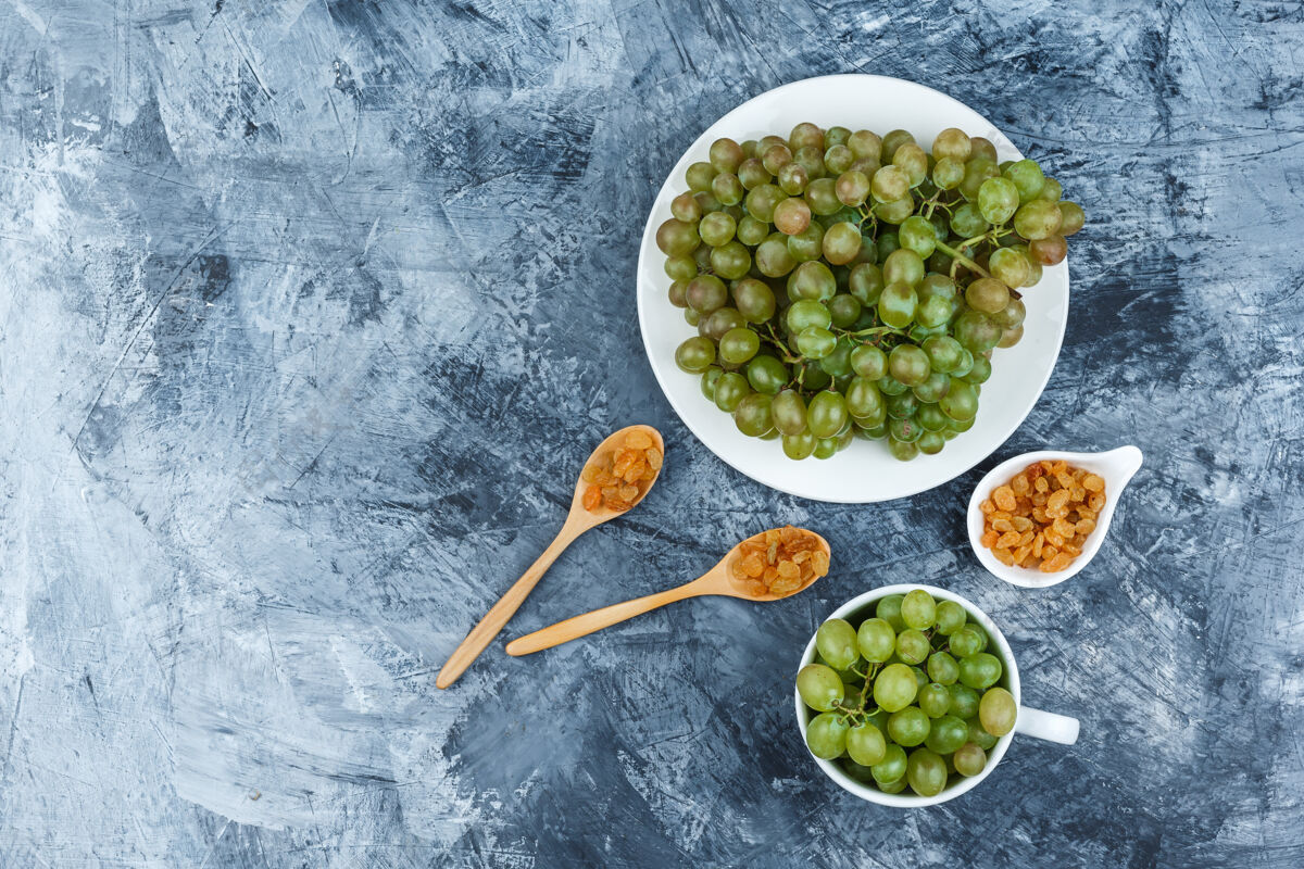水果顶视图绿色葡萄在白色盘子和杯子里 葡萄干在粗糙的石膏背景上水平杯子饮食健康