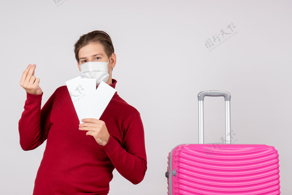 旅行白墙上戴着面具拿着飞机票的年轻男子的正视图人年轻男性举行