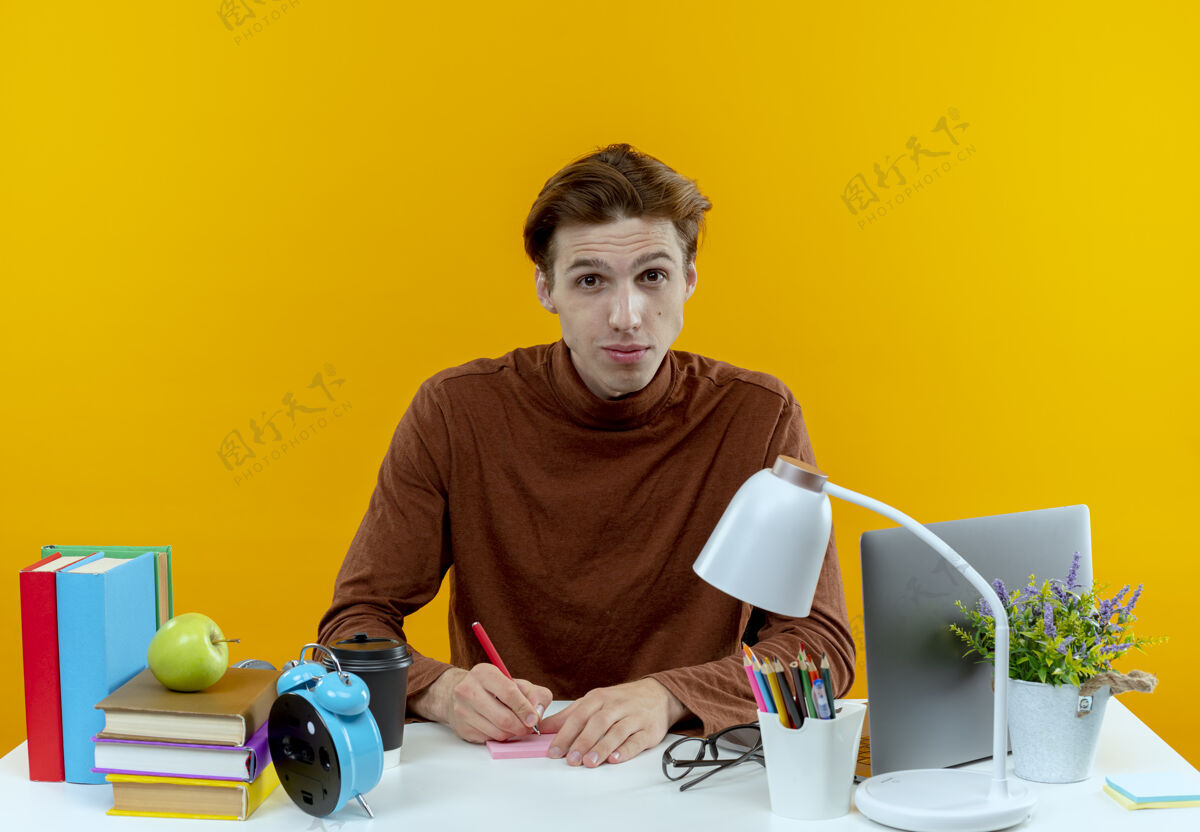 年轻坐在书桌旁拿着学习工具写东西的年轻学生男孩书桌坐着学校