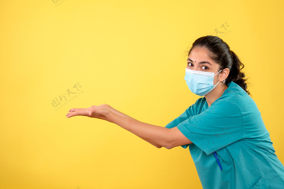 成人戴着医用面罩的年轻女医生在黄色的墙上张开双手人手开放