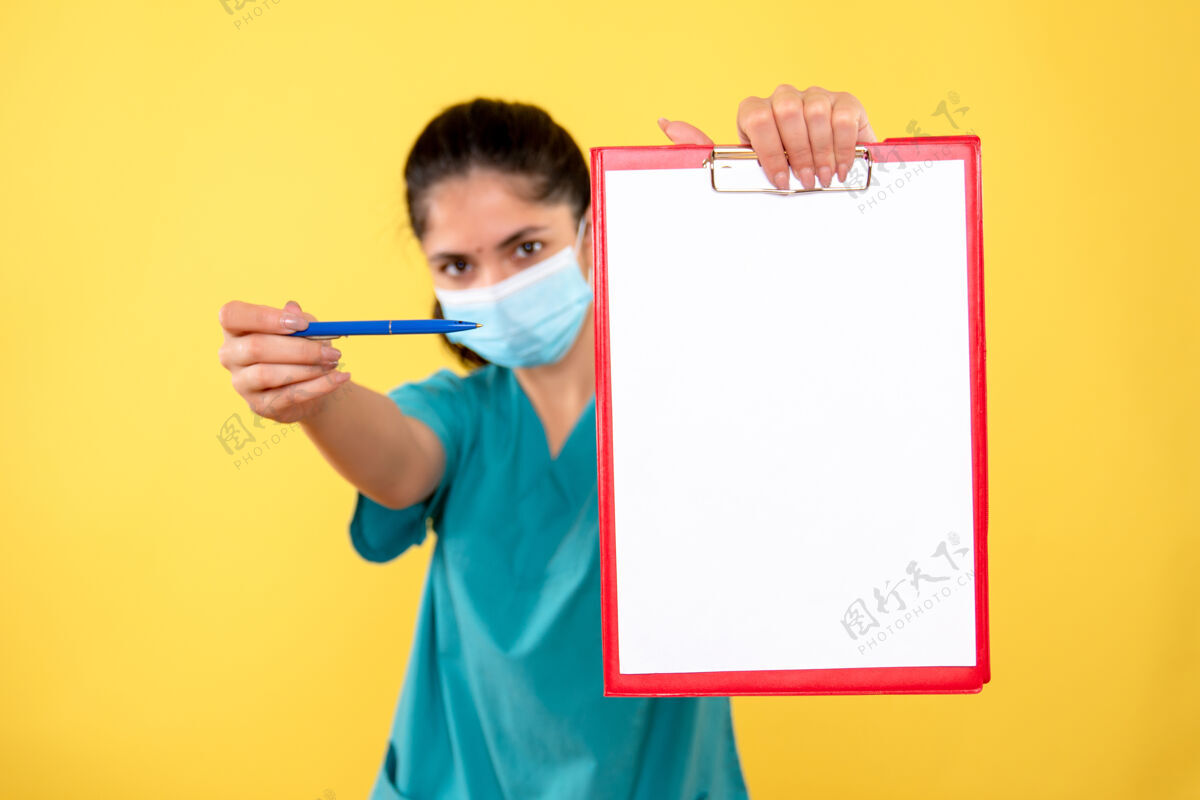 欢呼黄色墙壁上拿着剪贴板的戴着医用面罩的年轻女性的正视图剪贴板面具持有