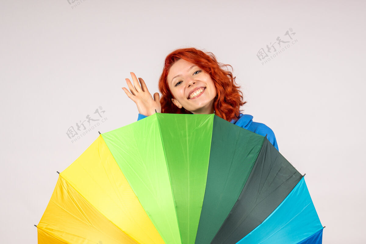 情绪白色墙壁上带着彩色雨伞的年轻女性的正视图年轻女性快乐雨