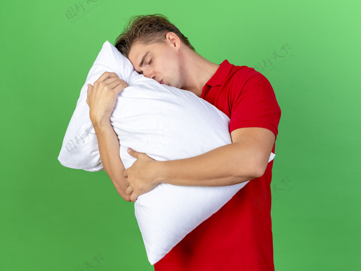 英俊年轻英俊的金发病男子抱着亲吻枕头闭着眼睛孤立在绿色的墙上疾病表达年轻
