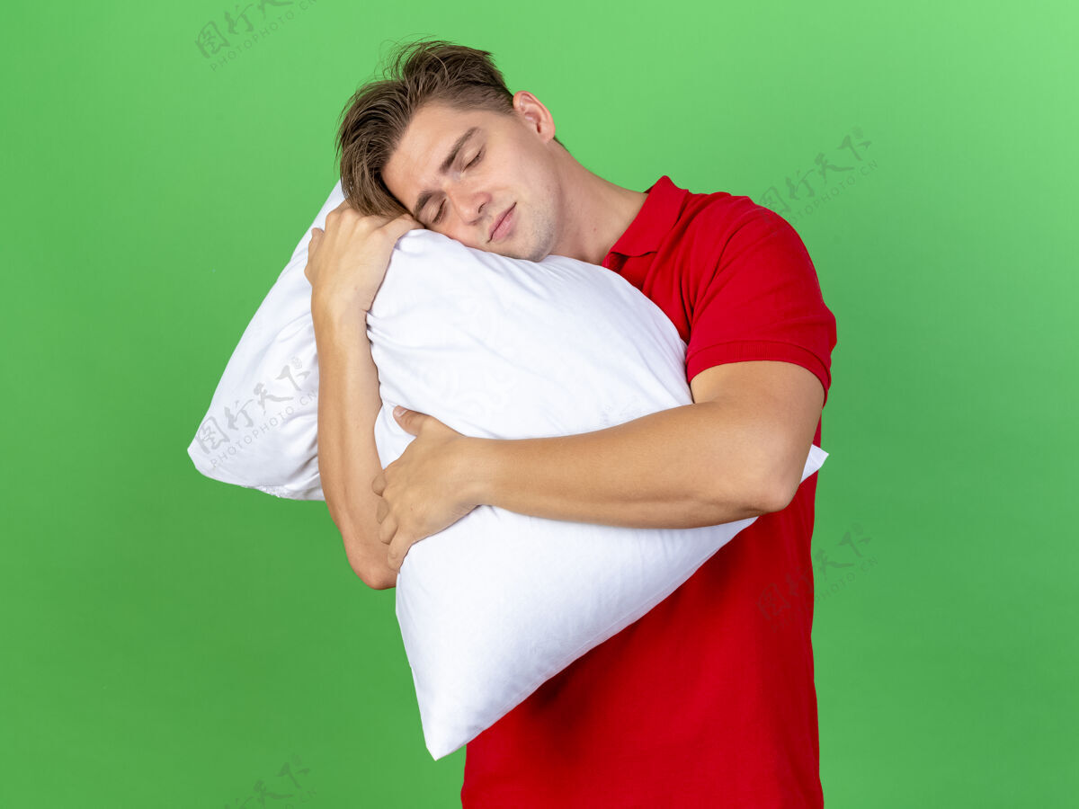 头高兴的年轻英俊的金发病男子抱着枕头把头放在它睡在绿色的墙壁上与复制sapce隔离表达请帅哥