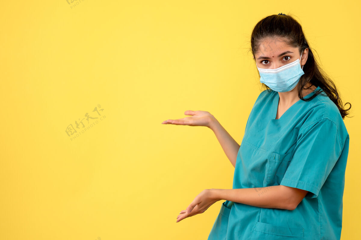 快乐戴着医用面罩的漂亮女医生正对着黄色墙上的东西微笑人人