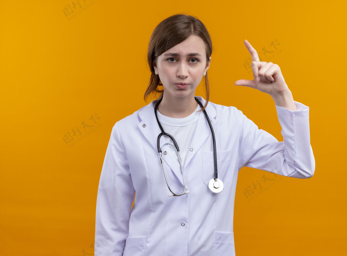 女士年轻的女医生穿着医用长袍和听诊器在隔离的橙色墙壁上做大小手势 还有复印空间尺寸年轻人医生