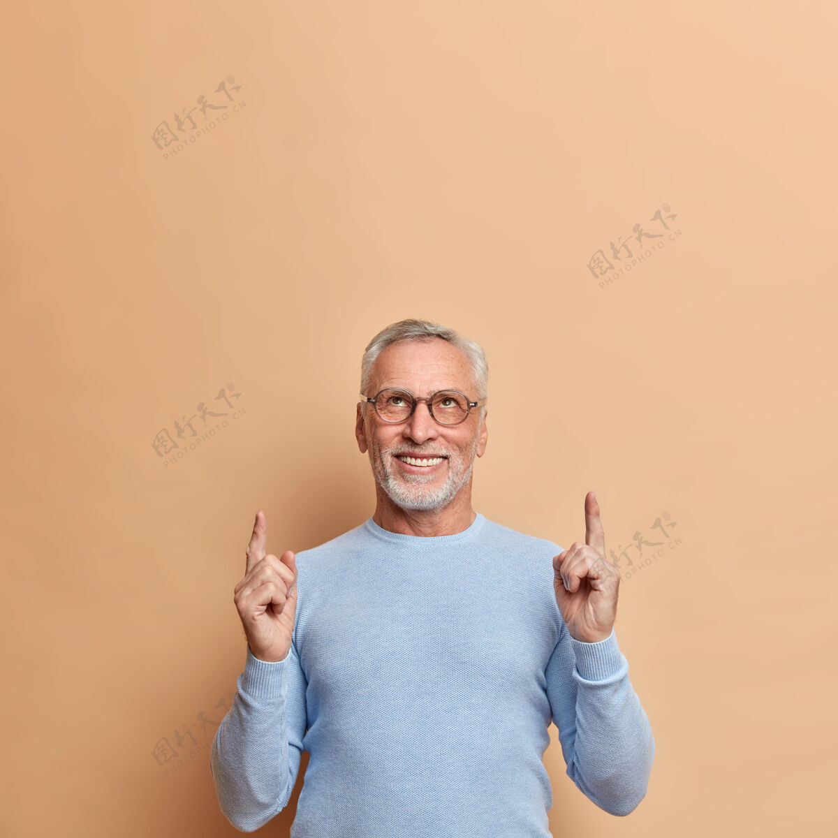 眼镜自信积极的成熟男人指着上面的空白处演示头顶上的广告 穿着休闲的蓝色套头衫 隔着棕色的墙壁镜头男人高兴