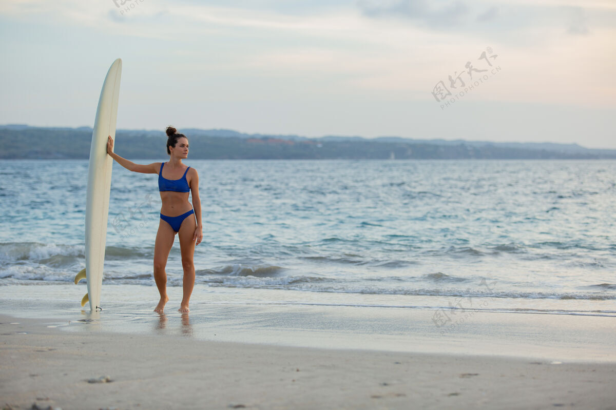 运动美丽的女孩拿着冲浪板站在沙滩上冲浪独自冲浪板