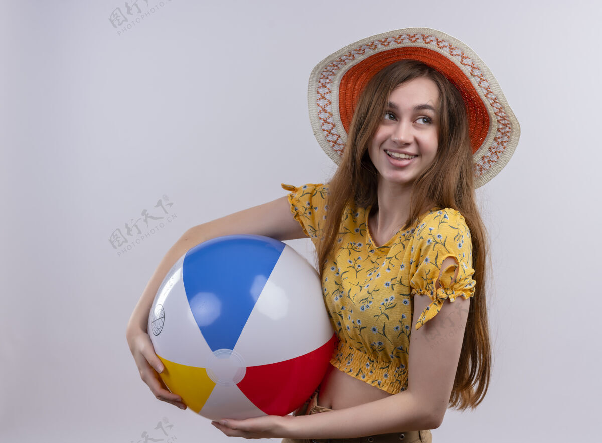 穿微笑的年轻女孩戴着帽子拿着沙滩球 看着右边孤零零的白色墙壁右侧身帽子