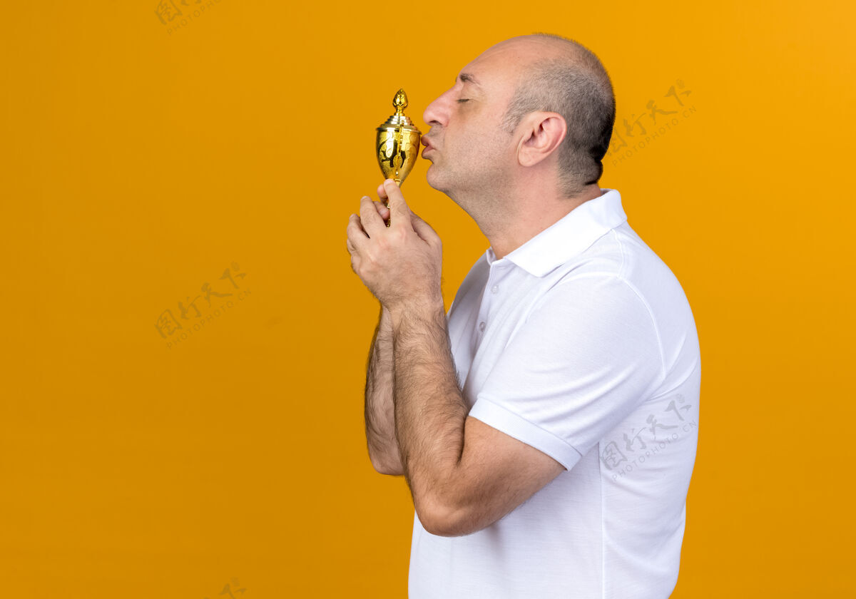 赢家站在侧视图随意成熟的男子举行和亲吻冠军杯隔离在黄色墙上复制空间立场看法个人资料