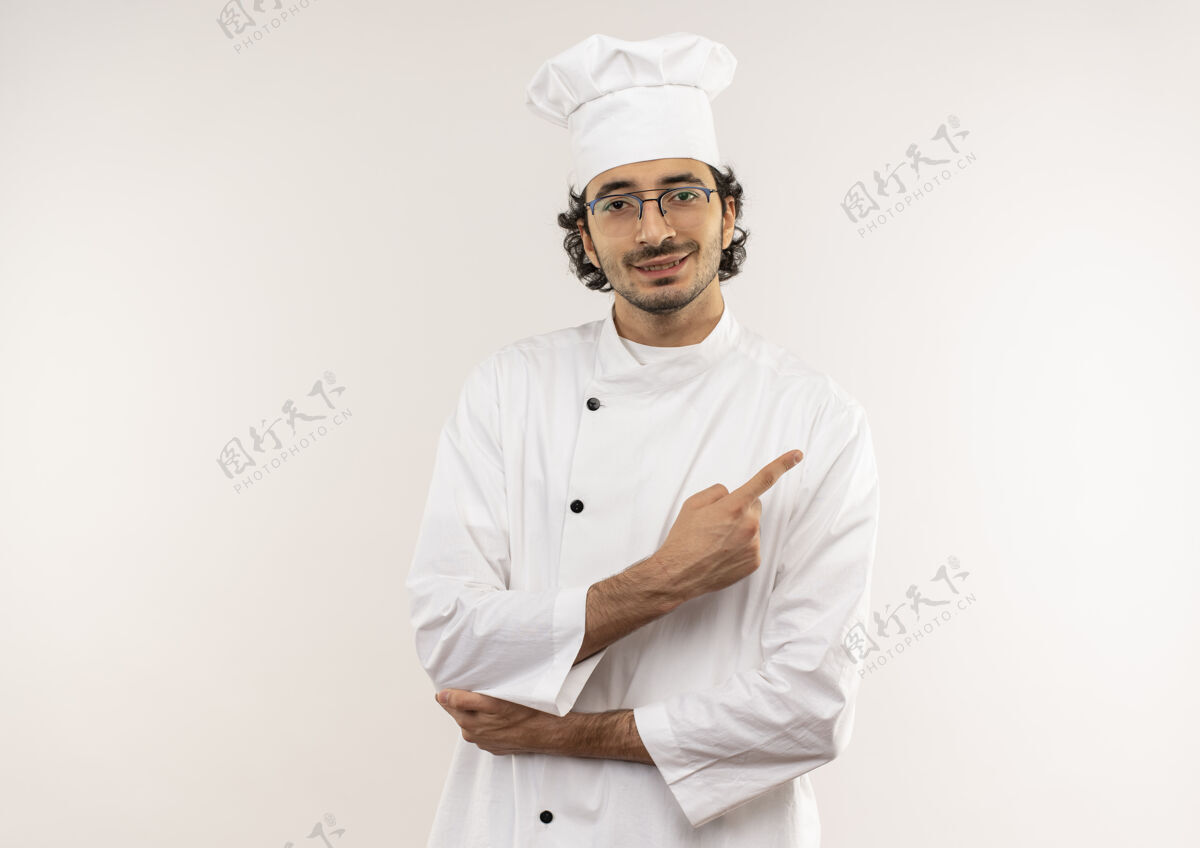 制服年轻的男厨师穿着厨师服 戴着眼镜 高兴地指着隔离在白色墙壁上的一侧 留着复印空间年轻请穿男