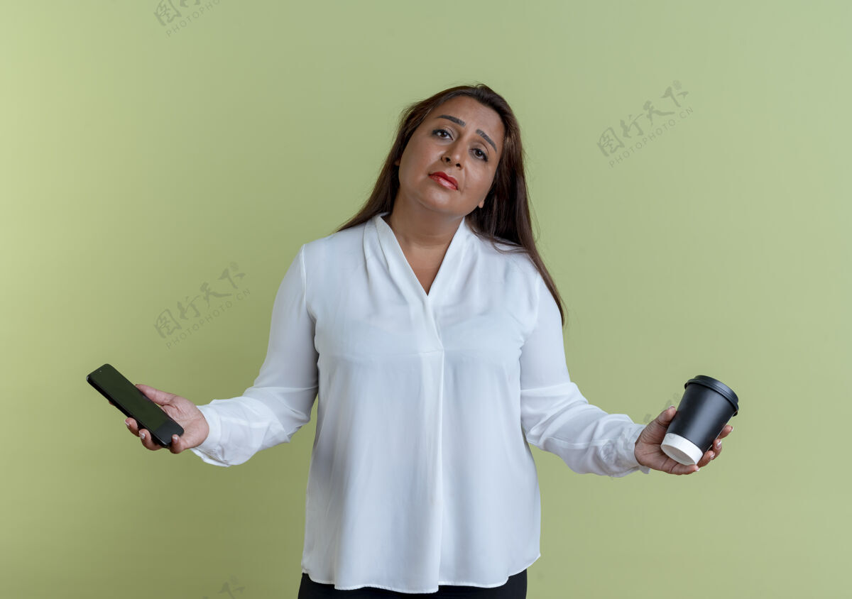 女人悲伤随意的高加索中年妇女手持电话 一杯咖啡孤立在橄榄绿的墙上持有咖啡杯子