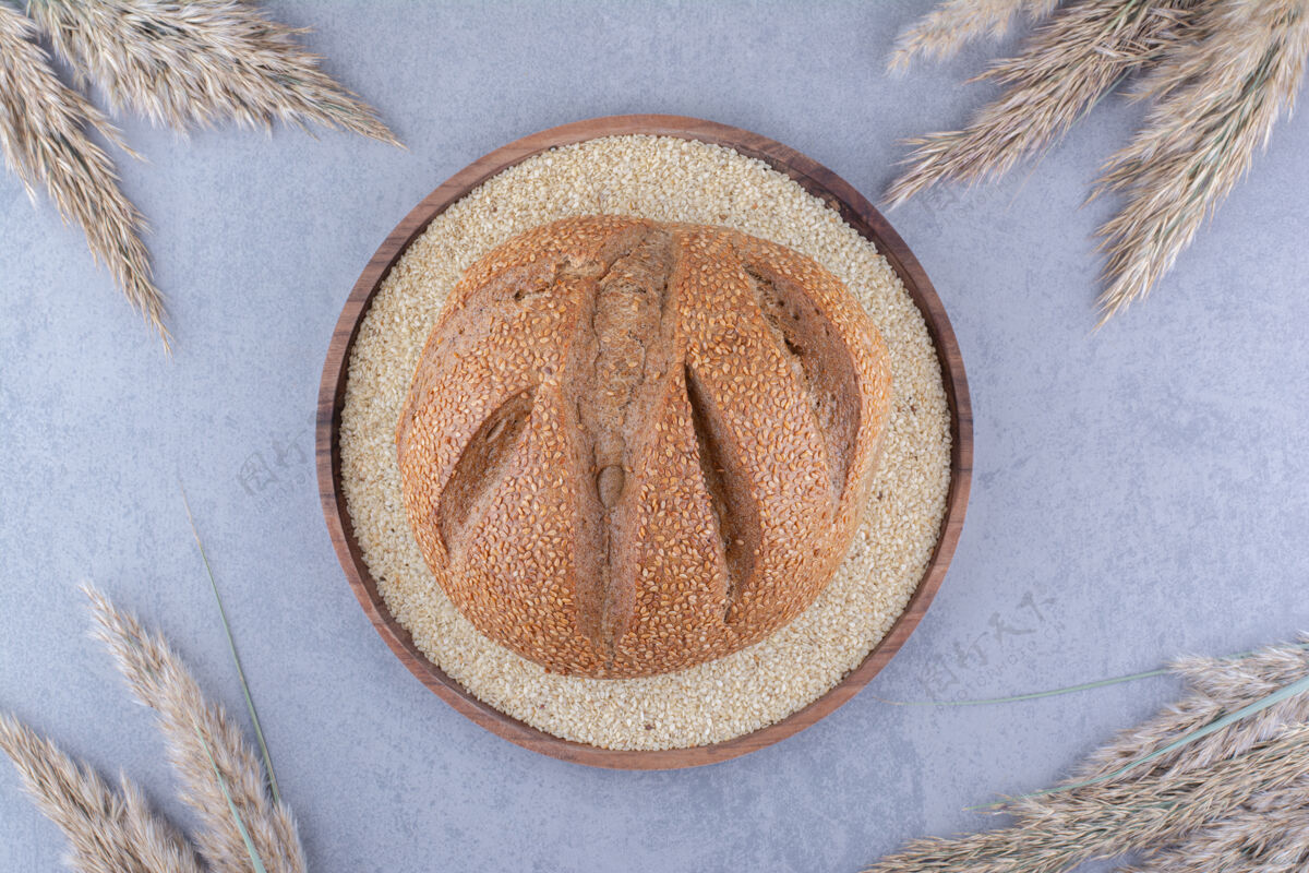 面团在一个装满芝麻籽的盘子里放一块面包 在大理石表面用干羽毛草茎围起来面包托盘面包屑