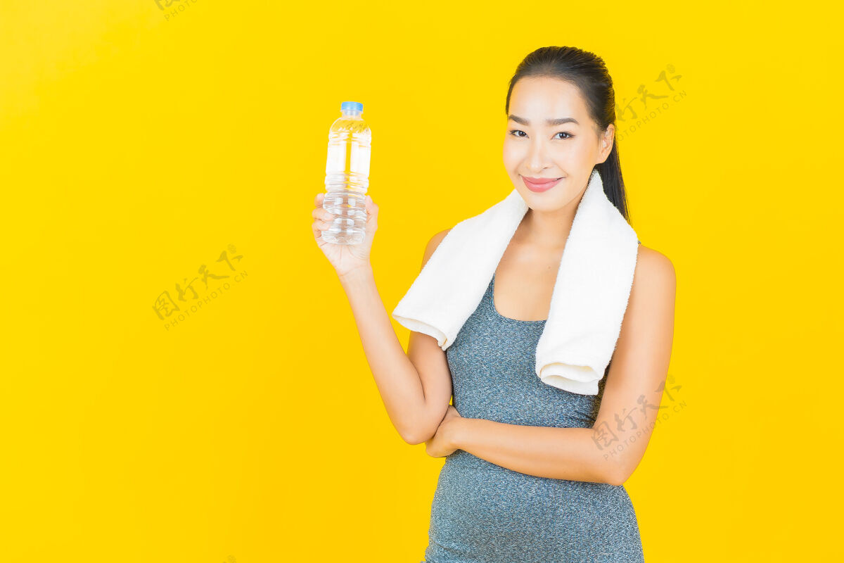 室内在黄色的墙上画一幅美丽的亚洲年轻女子 穿着运动服 喝着瓶装水饮食减肥漂亮
