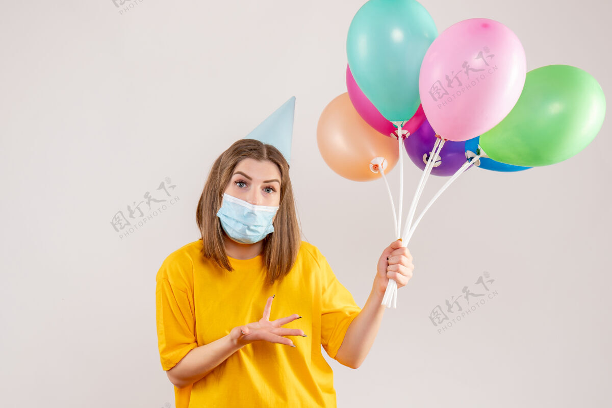 庆祝戴着白色面具手持彩色气球的年轻女性面具举行生日