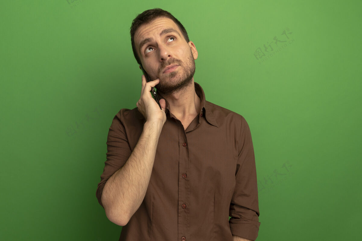 年轻人体贴的白人年轻人在电话里说话 在绿色的背景下 看着孤立的空间心想电话