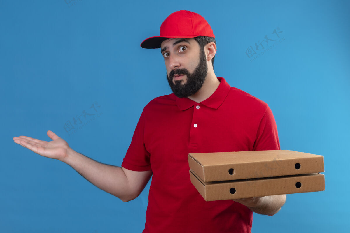 拿着年轻英俊的白人送货员穿着红色制服 戴着帽子 手里拿着披萨盒 手上空空的 蓝色的披萨帅哥空的