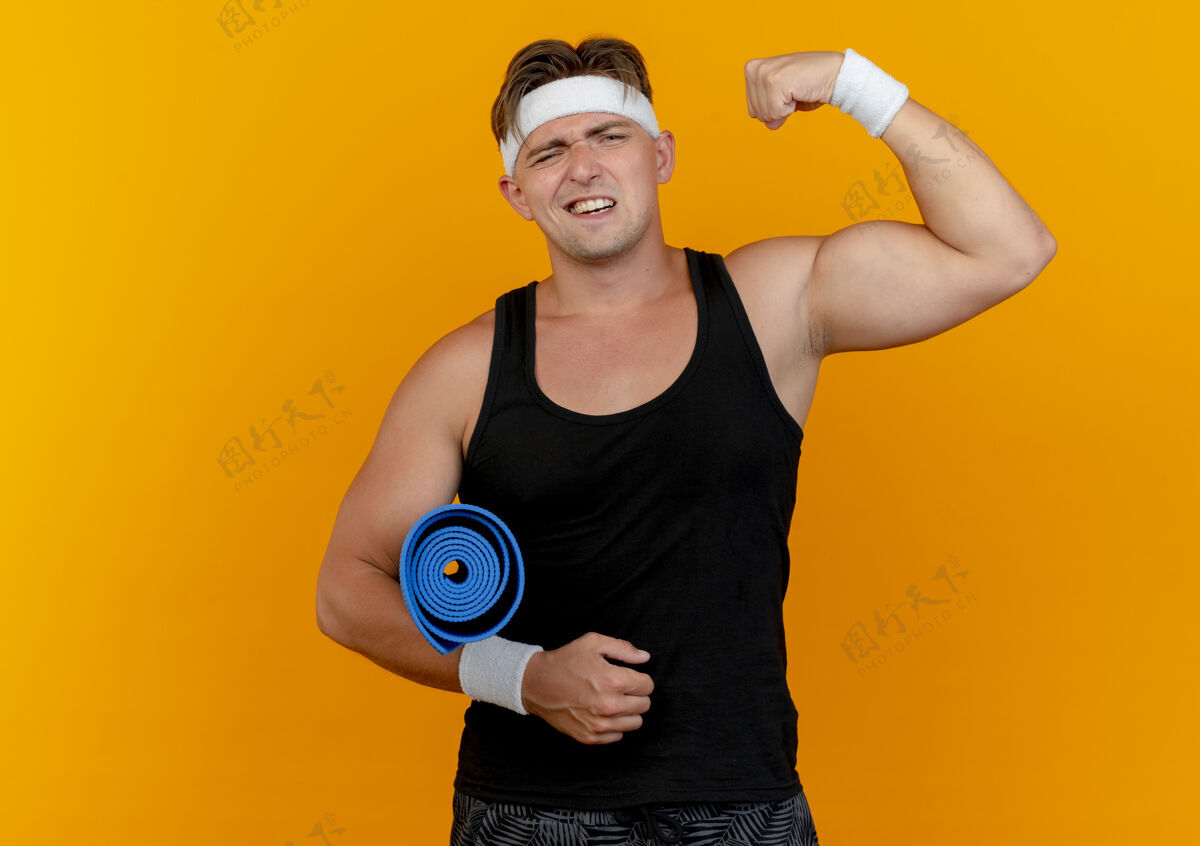 复制自信的年轻帅气的运动型男人戴着头带和腕带拿着毛巾 在橙色的空间里做着强烈的孤立的手势运动自信手势