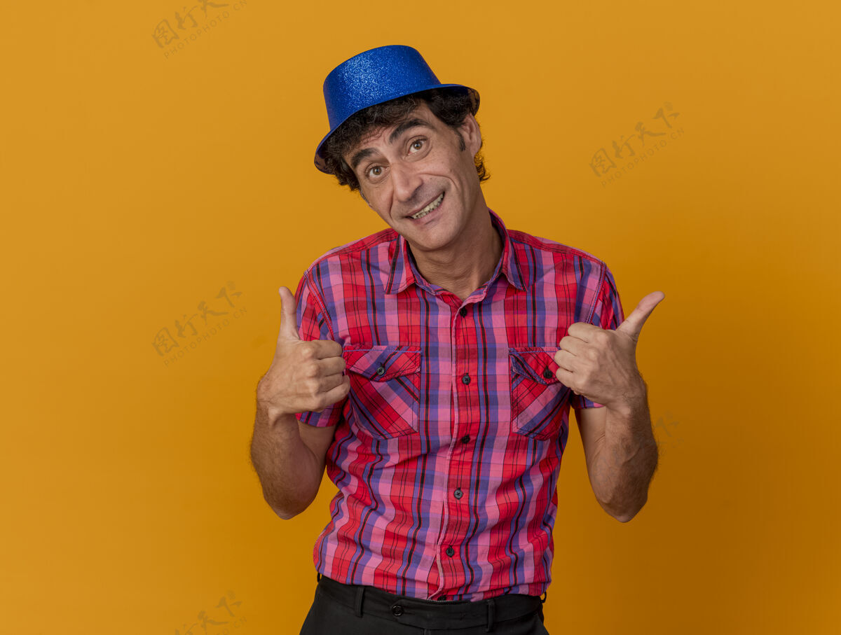拇指微笑的中年白种人党男子戴着党的帽子看着相机显示拇指向上孤立的橙色背景与复制空间帽子相机中年