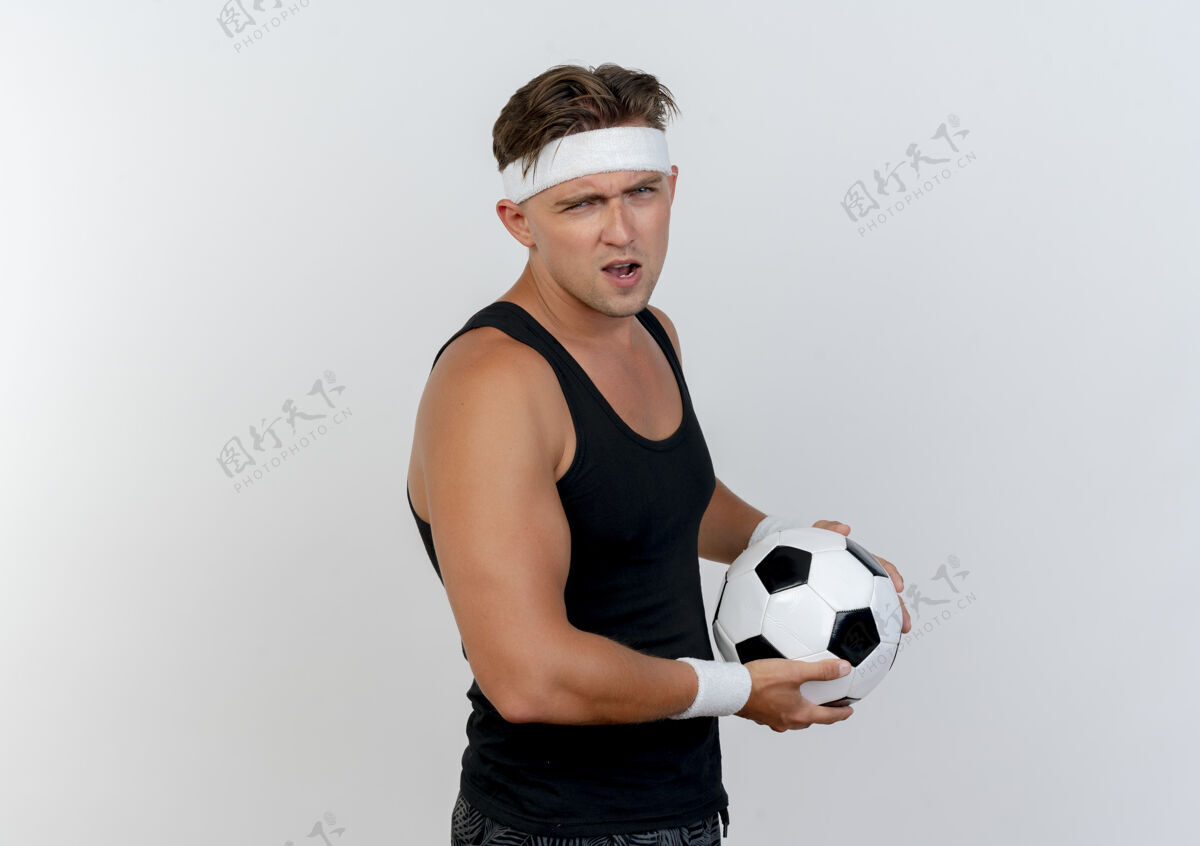持有自信的年轻帅气的运动型男人戴着头带和腕带拿着足球隔离在白色的复制空间运动空间复制