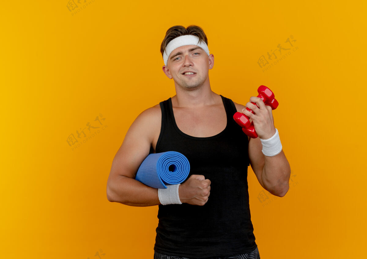 运动自信的年轻帅气的运动型男人戴着头带和手环拿着哑铃用毛巾隔离在橙色的复制空间年轻佩戴太空