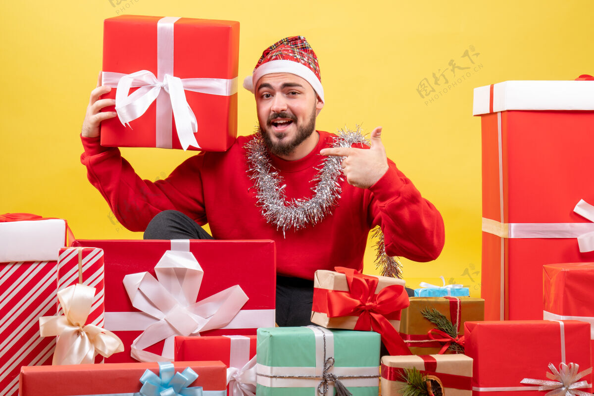 背景正面图：年轻男性围坐在黄色背景上的圣诞礼物旁礼物冬天礼物