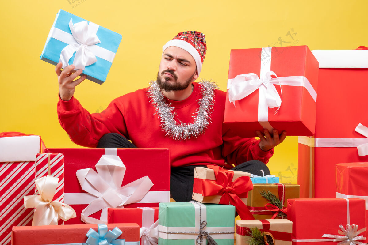 购物正面图：年轻男性围坐在黄色背景上的圣诞礼物旁坐着礼物年轻的男性