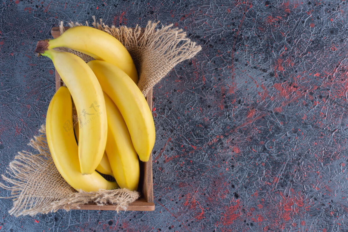 健康一堆新鲜的香蕉放在木箱里 放在五颜六色的表面上新鲜簇生