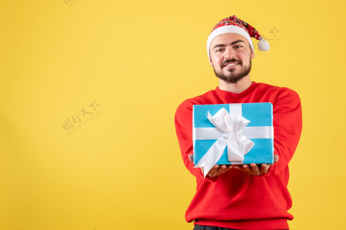 礼物正面图黄色背景上手持圣诞礼物的年轻男性人年轻男性年份