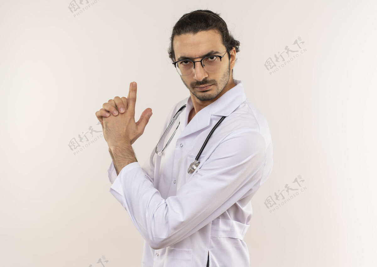 严格的年轻男性医生 戴着眼镜 穿着白色长袍 手持听诊器 在隔离的白色墙壁上用做手势 留有复印空间长袍男性眼镜