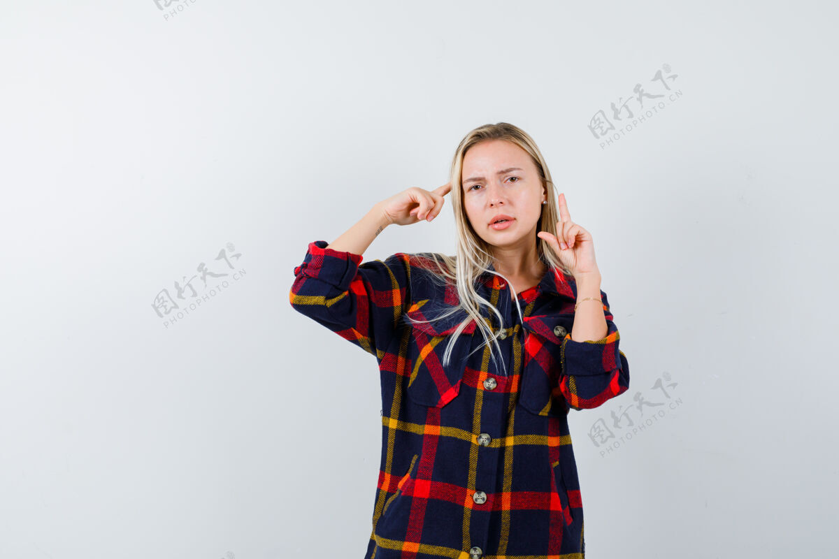 干净年轻的女士站在思考的姿势 同时指出在格子衬衫 并期待犹豫不决 前视图犹豫女性完美