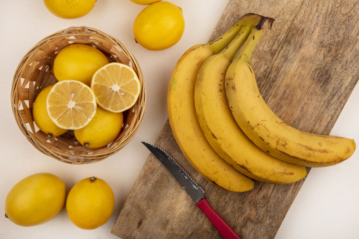 桶顶视图黄色皮肤的柠檬桶香蕉孤立在一个木制的厨房板与刀上的白色墙壁视图板新鲜