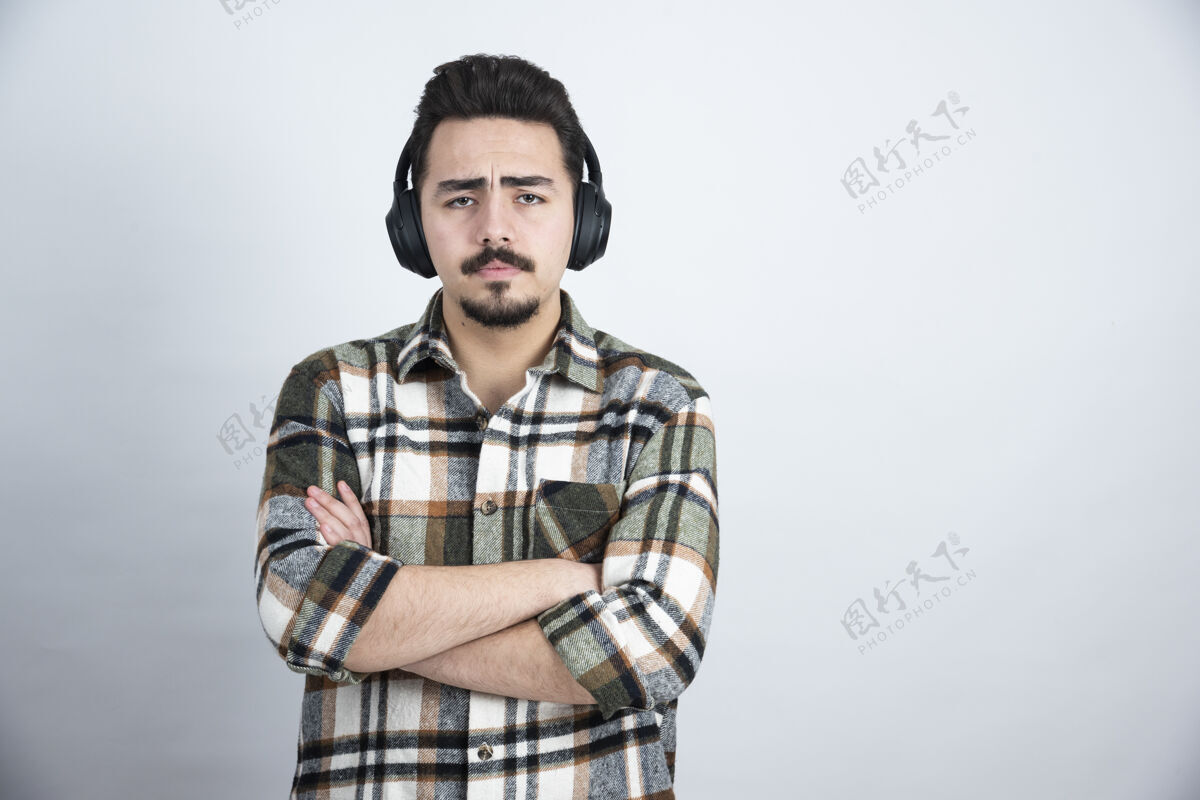 音乐戴着耳机在白墙上听音乐的帅哥享受声音年轻人