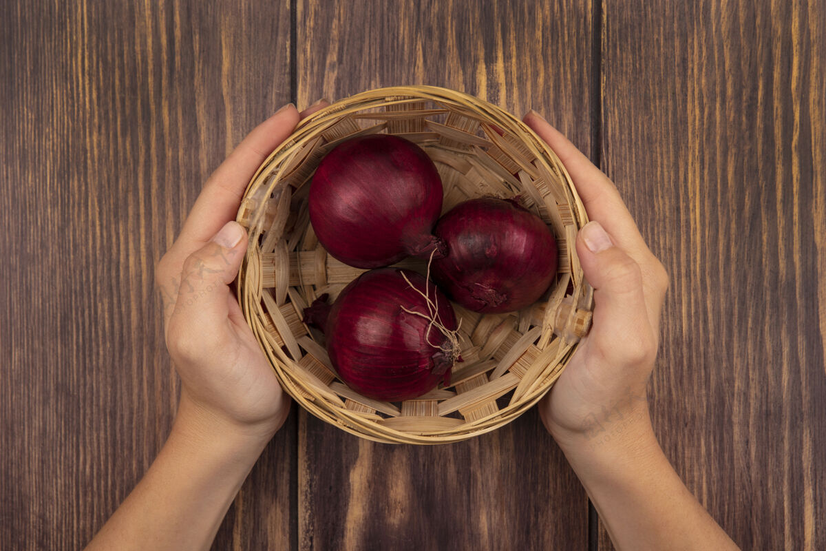 食物顶视图：女性手拿着一碗健康的红洋葱放在木墙上新鲜的木头餐
