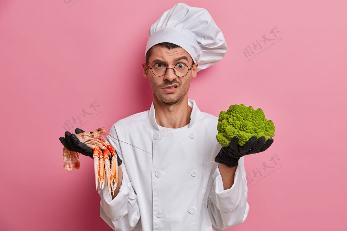 食物不高兴的厨师穿着白色制服 在餐厅工作 被指派用西兰花和小龙虾做菜 戴着黑色手套产品烹饪粉色