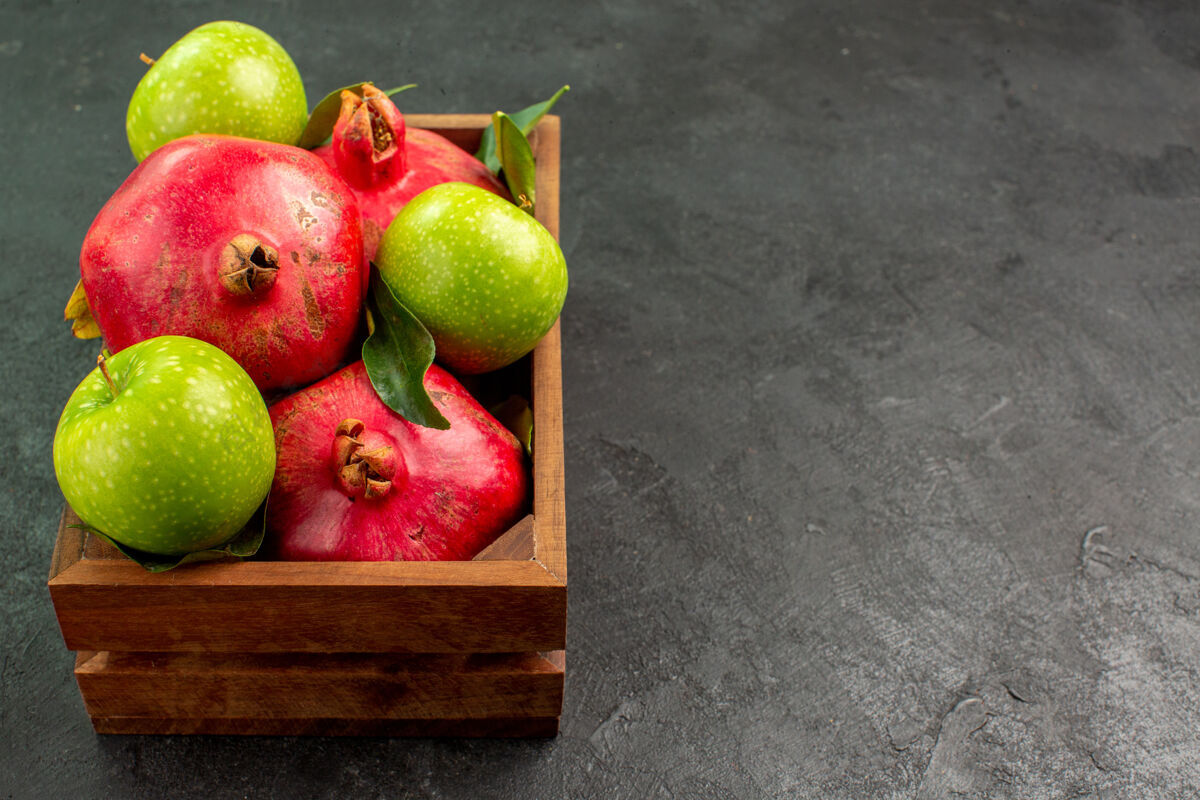 吃苹果正面是新鲜的红石榴和青苹果 深色的桌子上有成熟的水果色新鲜农产品梨