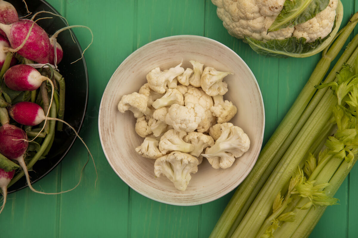 食品顶视图新鲜的花椰菜小花在一个碗与萝卜在一个碗与整个花椰菜和芹菜隔离在一个绿色的木墙上观点萝卜新鲜