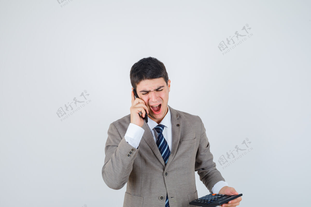 不高兴小男孩在打电话 穿着正装拿着计算器 看上去很烦躁前视图电话年轻男人