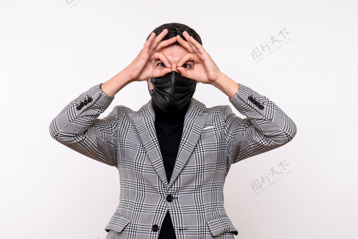 前面正面图：戴着黑色面具的年轻人站在白色孤立的背景上 把奥基标志放在眼前眼睛套装视图