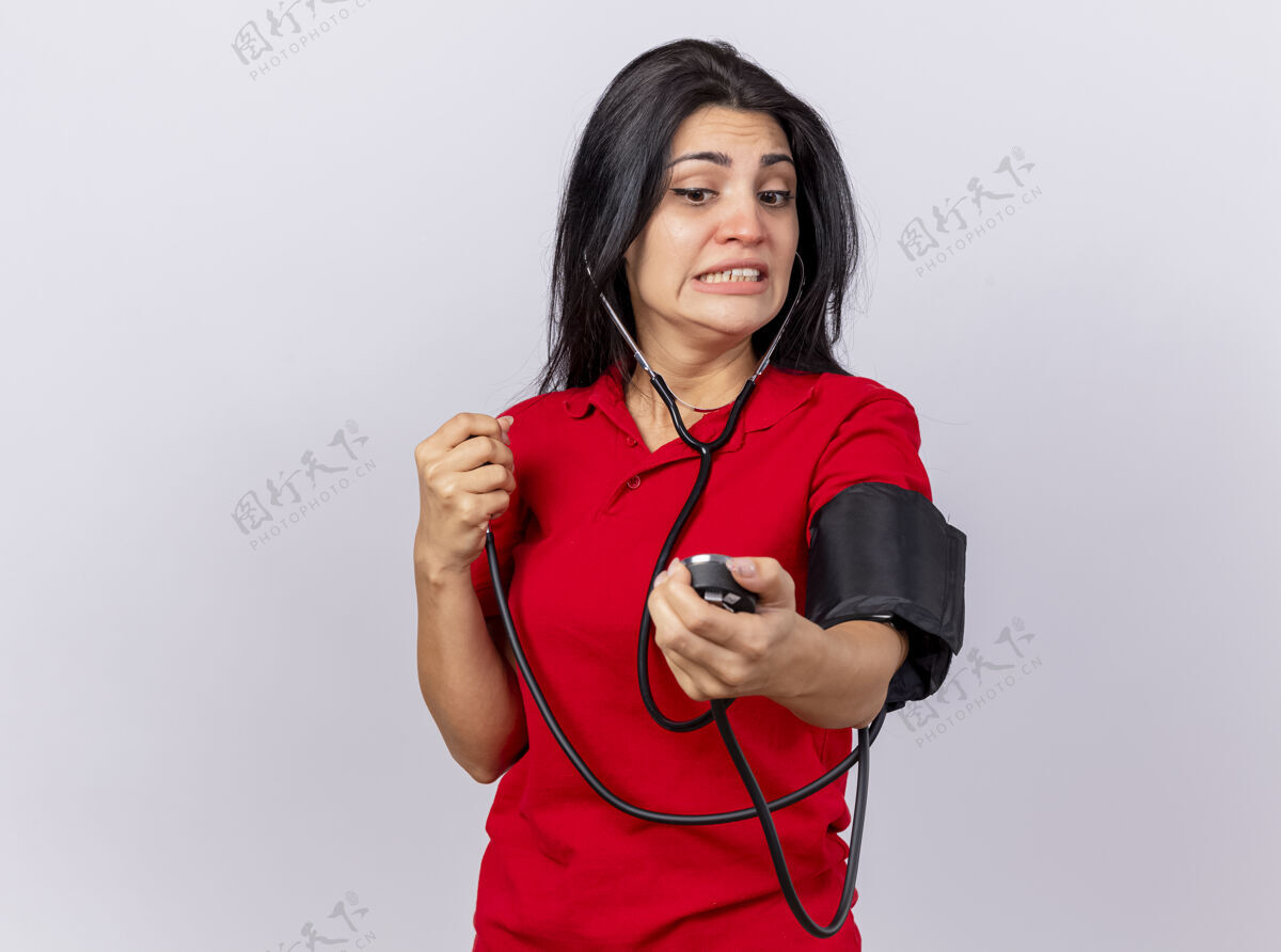 女孩焦虑的年轻白人女孩戴着听诊器 用血压计测量她的血压 在白色背景上 用复制空间孤立地看着它佩戴压力年轻