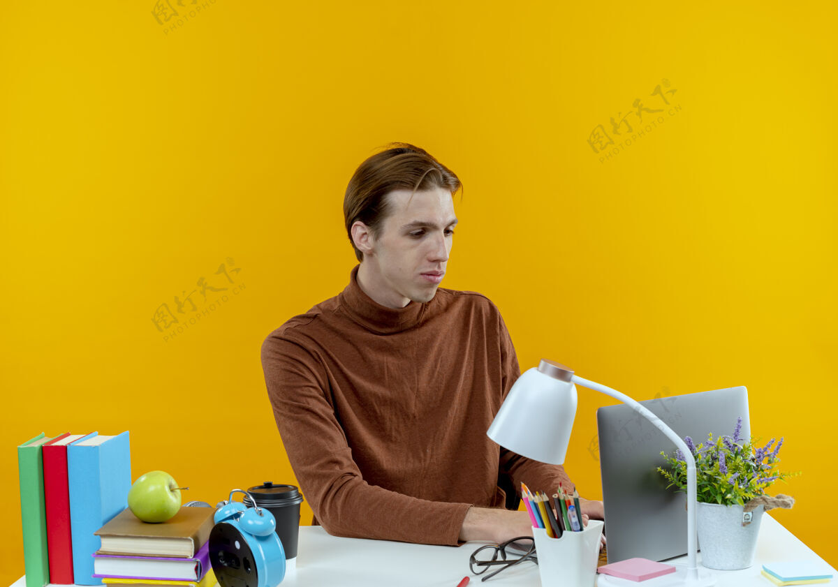 黄色高兴的小男孩坐在书桌旁 用黄色笔记本电脑上的学习工具学校学生男孩