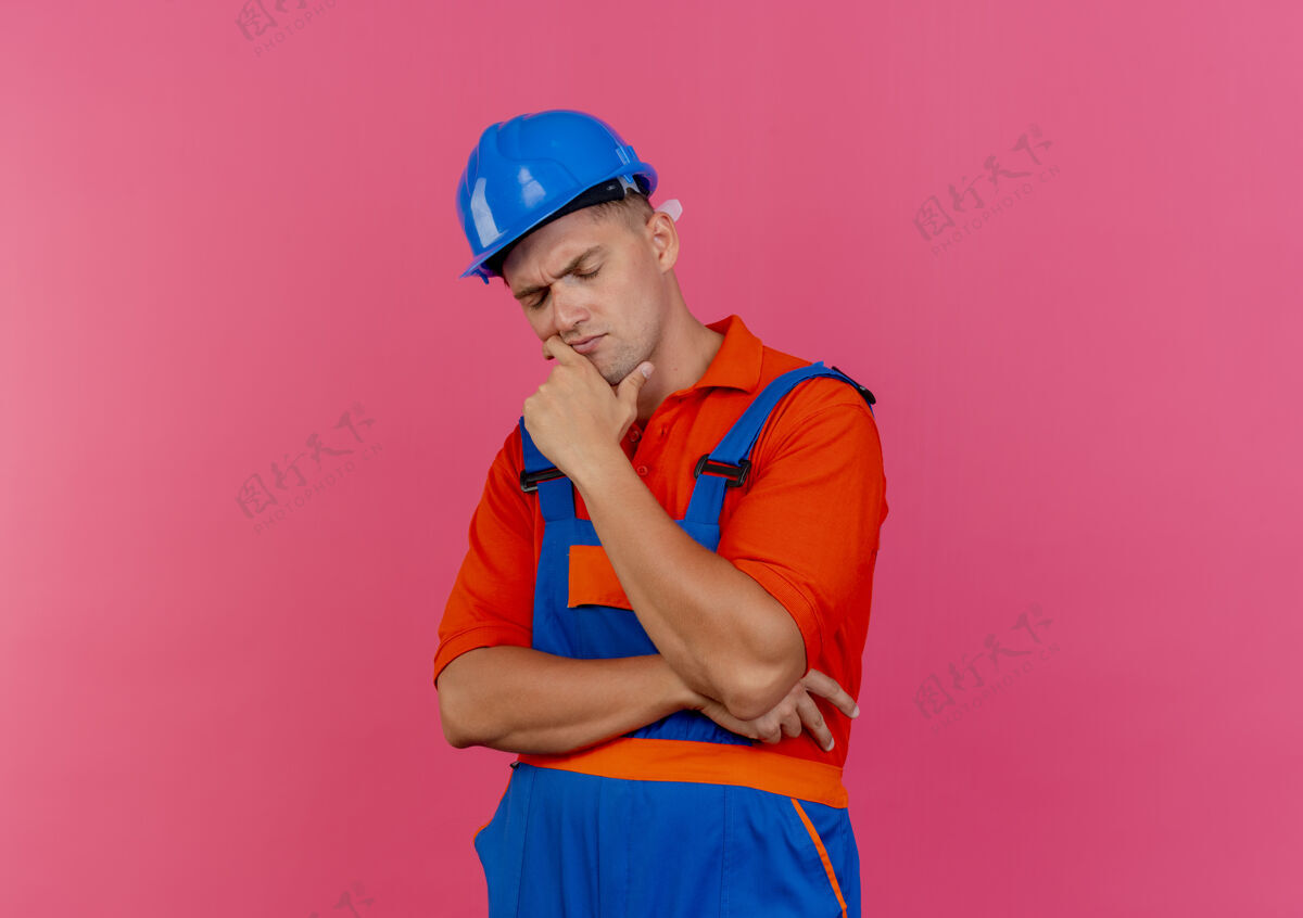 安全闭上眼睛思考穿着制服和安全帽的年轻男性建筑工人把手放在下巴下面的粉红色男性闭嘴建筑工人