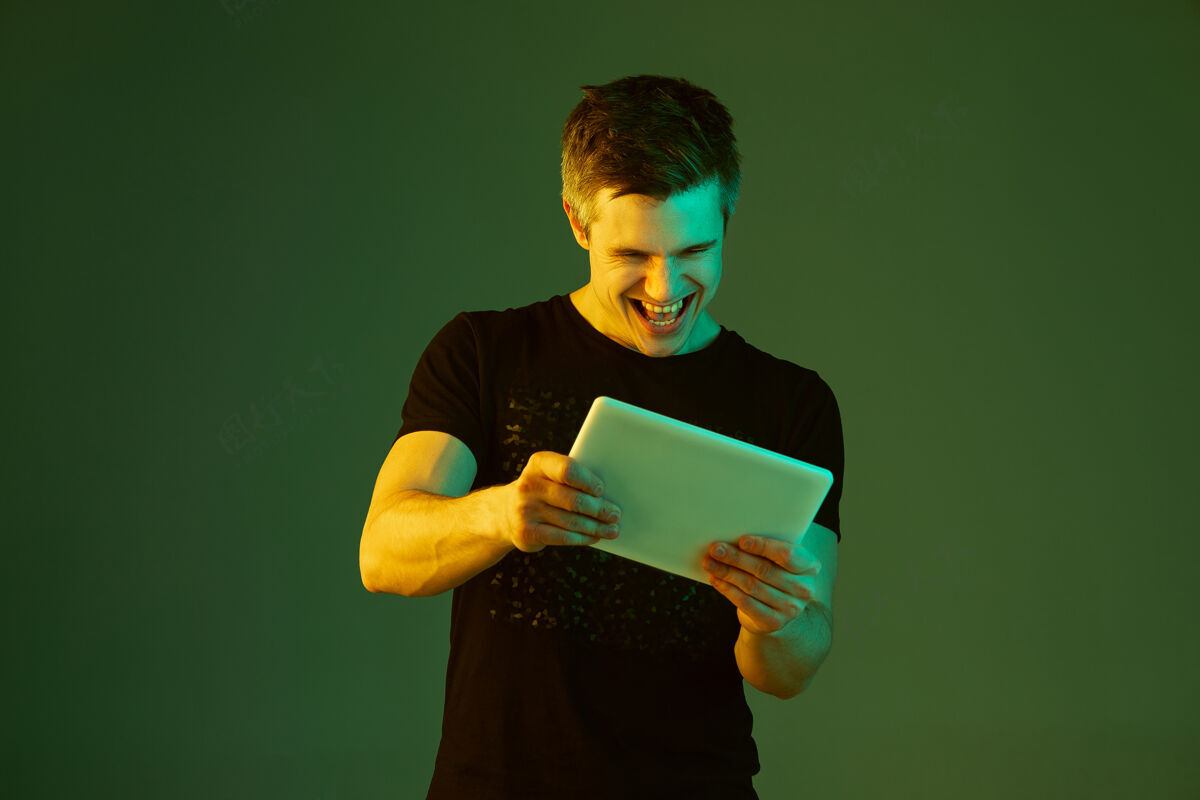 男人玩平板电脑白种人的肖像隔离在霓虹灯下的绿色背景上面部工作霓虹灯