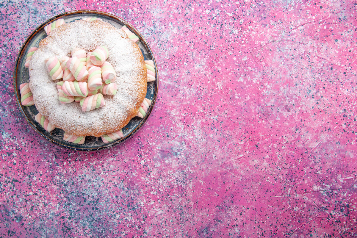 美味粉红色表面上糖粉蛋糕和甜棉花糖的俯视图糖棉花糖年龄