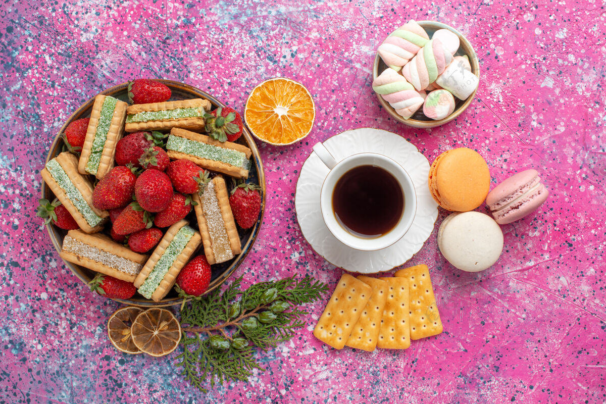 烘焙俯瞰美味的华夫饼与一杯茶马卡龙和新鲜的红色草莓粉红表面水果茶食物