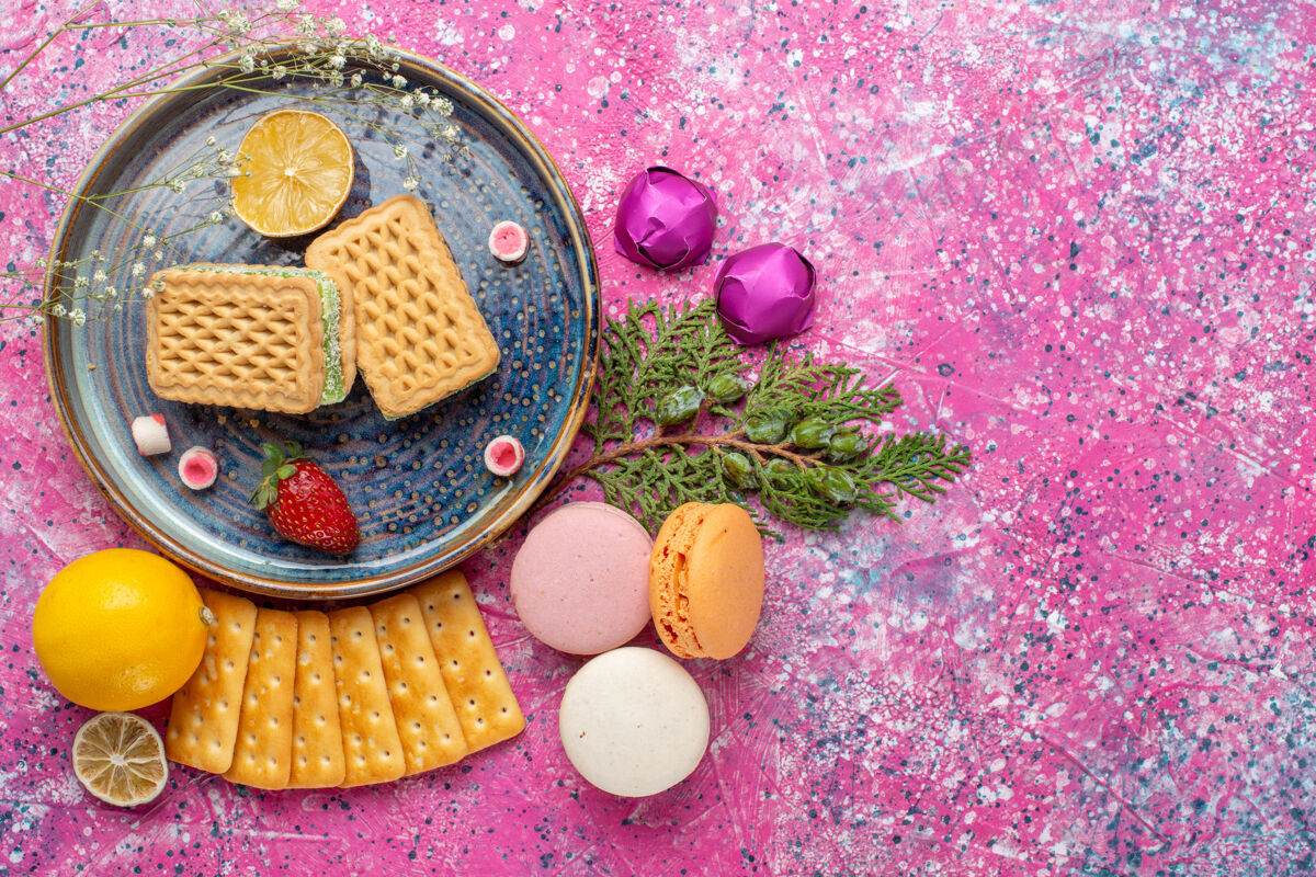 华夫饼粉红色表面上有美味的华夫饼和法国马卡龙饼干的俯视图糖果化妆品食品