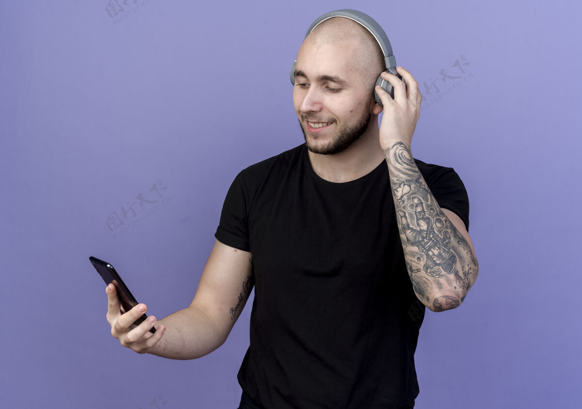 年轻高兴的年轻人戴着耳机 拿着手机看着紫色的隔离请戴耳机紫色
