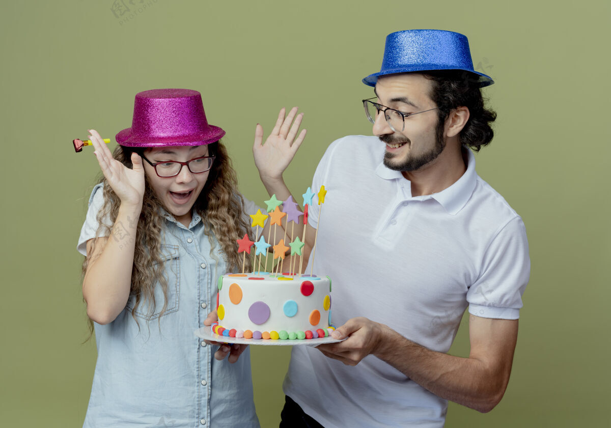 生日一对戴着粉蓝相间帽子的年轻人微笑着给被隔离在橄榄绿上的惊喜女孩送生日蛋糕粉色惊喜微笑