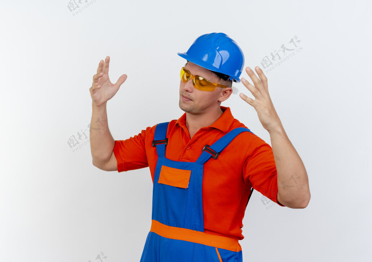安全戴着制服 安全帽和安全眼镜的疲惫的年轻男性建筑工人闭上眼睛 双手摊开男性白色眼镜